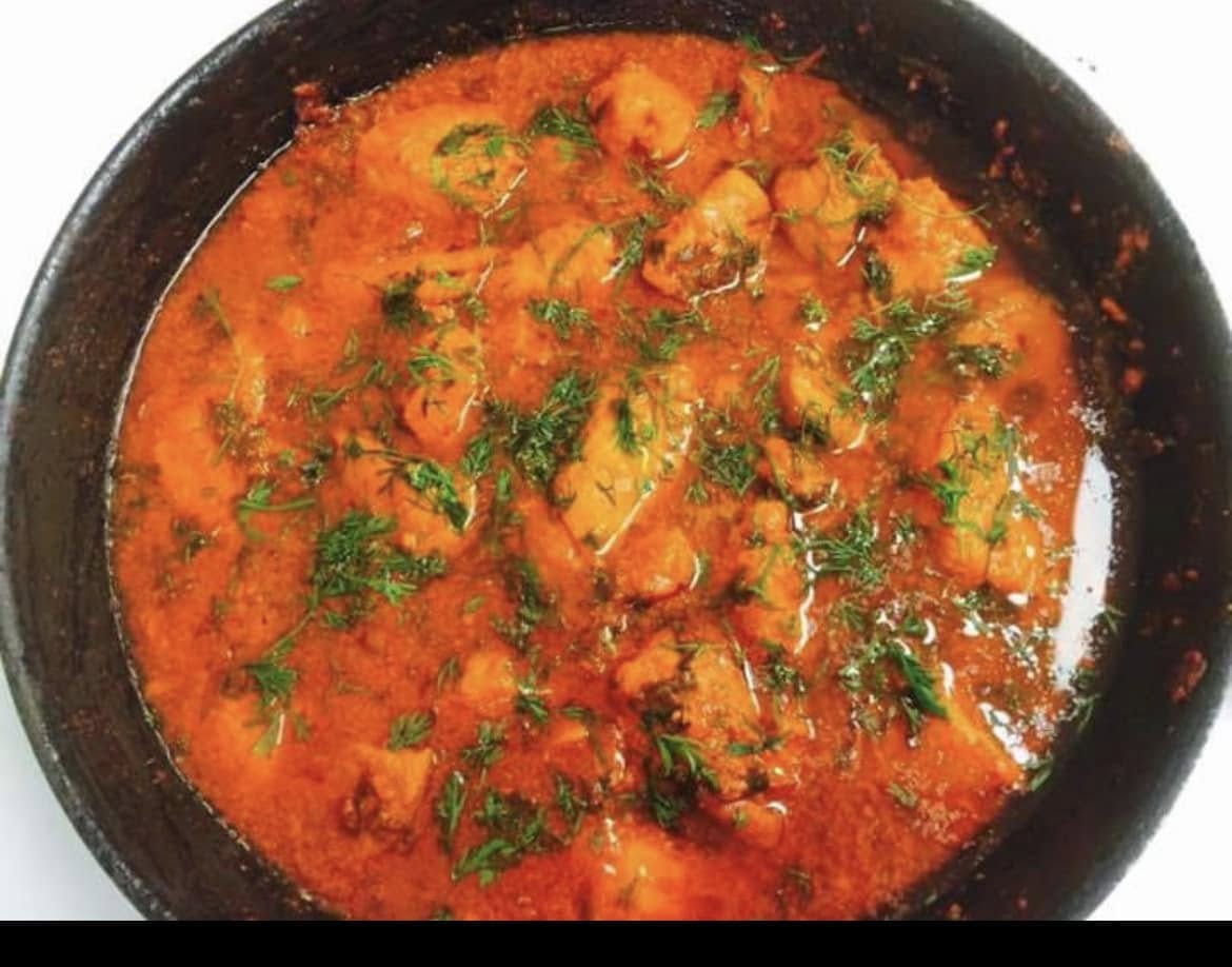 Chicken curry simmering in a black pan, topped with fresh herbs, at Desi Meal