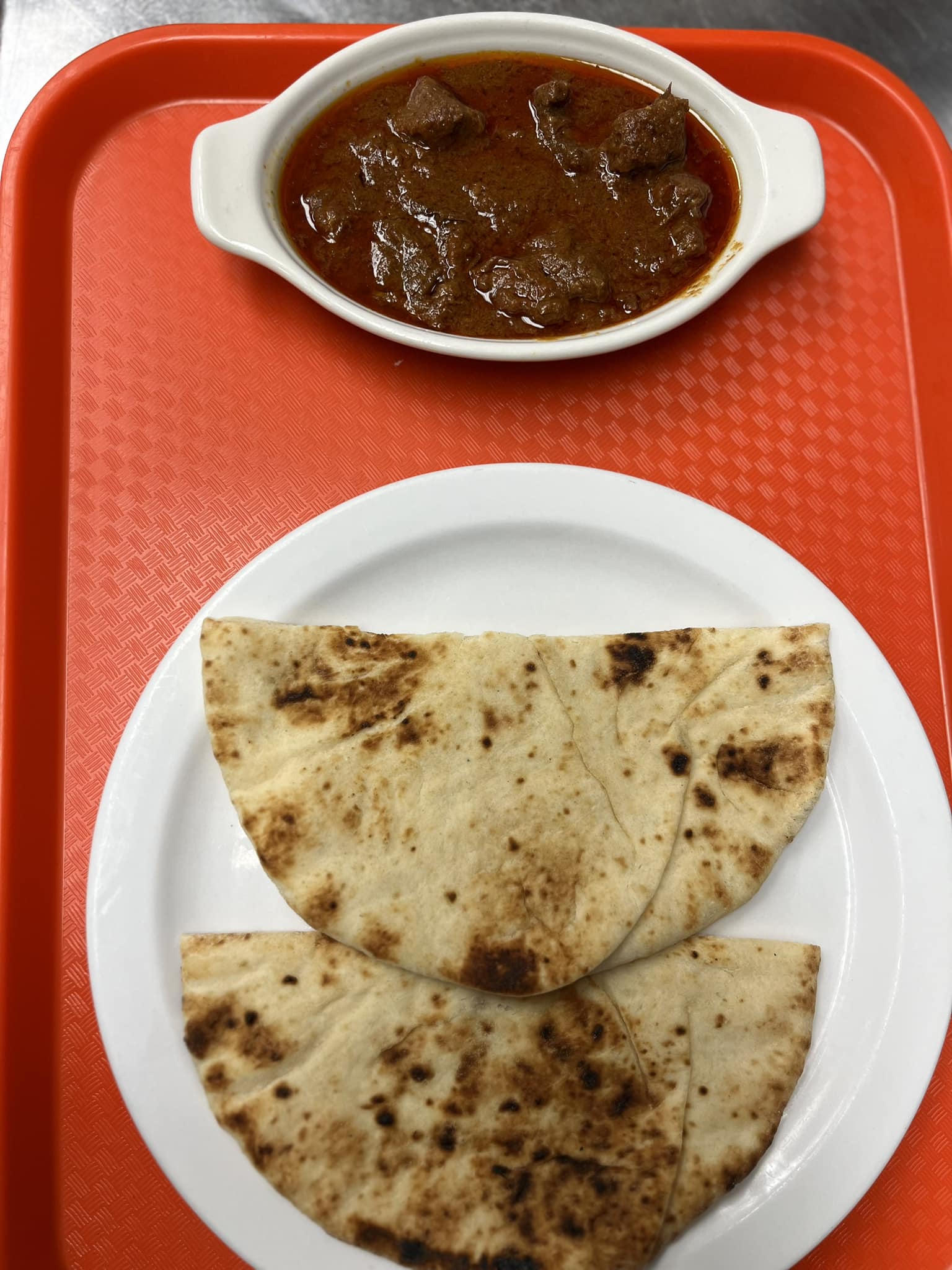 Bowl of beef curry with two pieces of fresh naan on a red tray