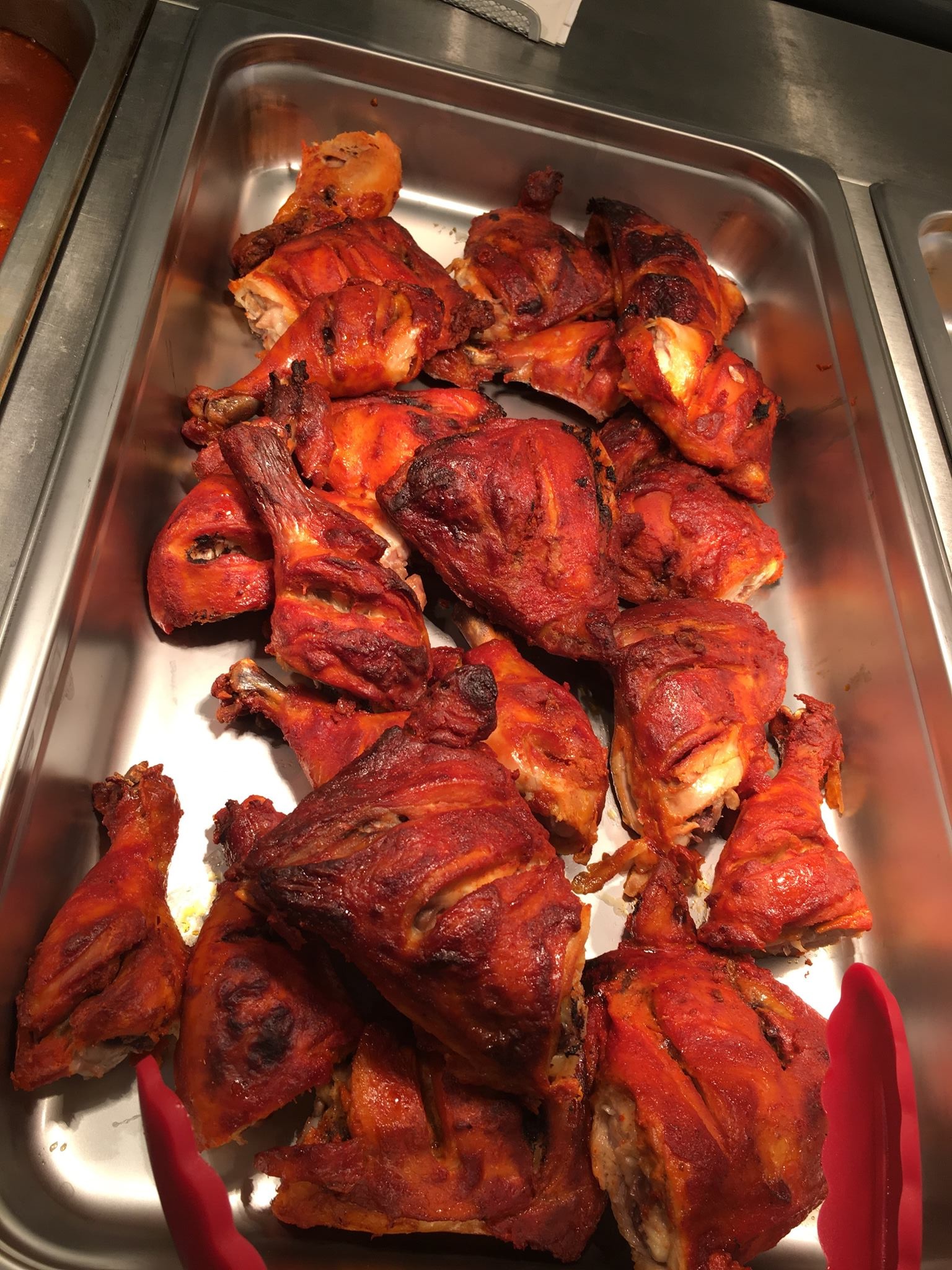 Metal tray of red-marinated tandoori chicken pieces